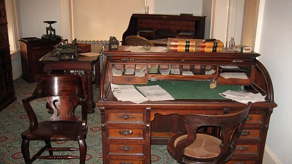 A fountain pen resting on a stack of unopened folded documents beside a plain brass desk lamp