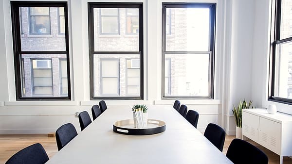 An empty conference chair pushed back from a table where a closed folder and a water glass remain in place.