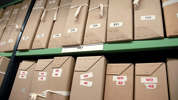 Numerous paper file folders arranged in overlapping rows across a large table, edges fanned out