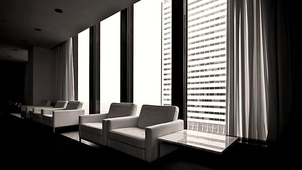 Two chairs facing each other across a bare table in a plain meeting room with a window at one end.