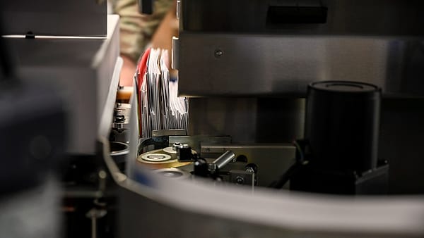 Sorted envelopes stacked in open mail trays on a metal sorting table under overhead lighting