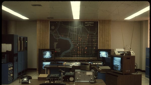 Two identical whiteboards in adjoining rooms seen through an open doorway, one wiped clean and one covered in notes.
