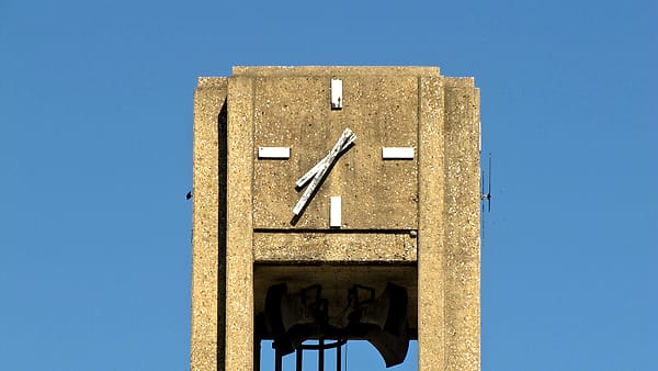 A wall calendar with a single square circled in red hanging beside a hard hat on a plain painted wall