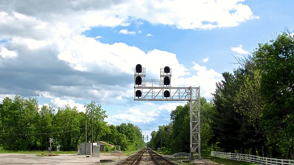 Three parallel railway tracks converging toward a distant switch under an overcast sky