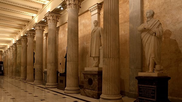 A long marble corridor with tall arched windows and a polished stone floor reflecting the daylight from outside.