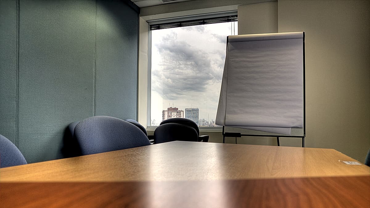Two chairs pulled up to one side of a bare wooden table with a single closed notebook between them
