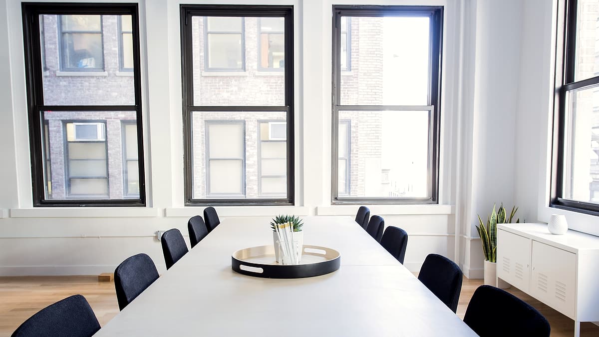 An empty conference chair pushed back from a table where a closed folder and a water glass remain in place.