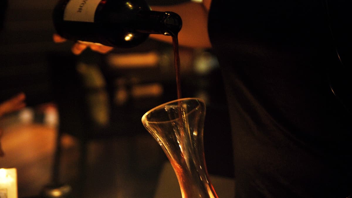 Wine being poured slowly from one glass carafe into a second carafe on a plain kitchen counter