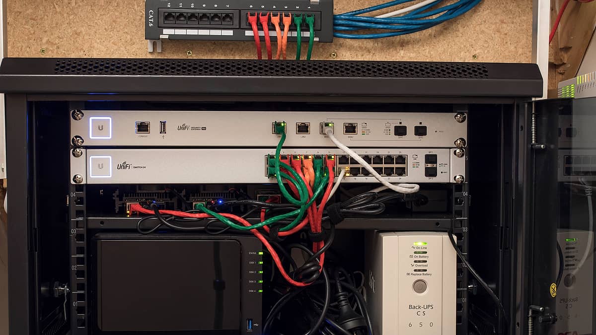 A server cabinet with cabling routed through a vertical channel, indicator lights showing in a dim room.