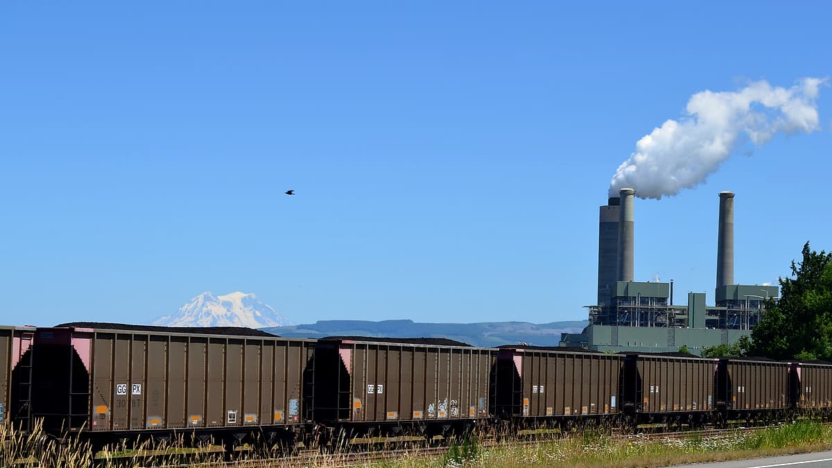 A conveyor belt carrying dark coal toward a tall storage silo under a flat gray sky