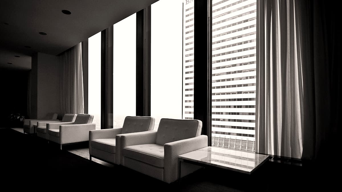Two chairs facing each other across a bare table in a plain meeting room with a window at one end.