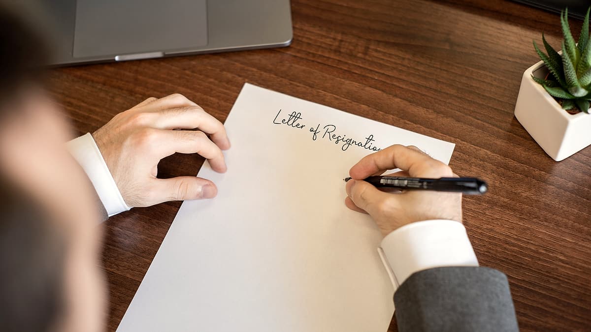 A plain white envelope and a folded letter lying on a wooden table beside a pair of reading glasses