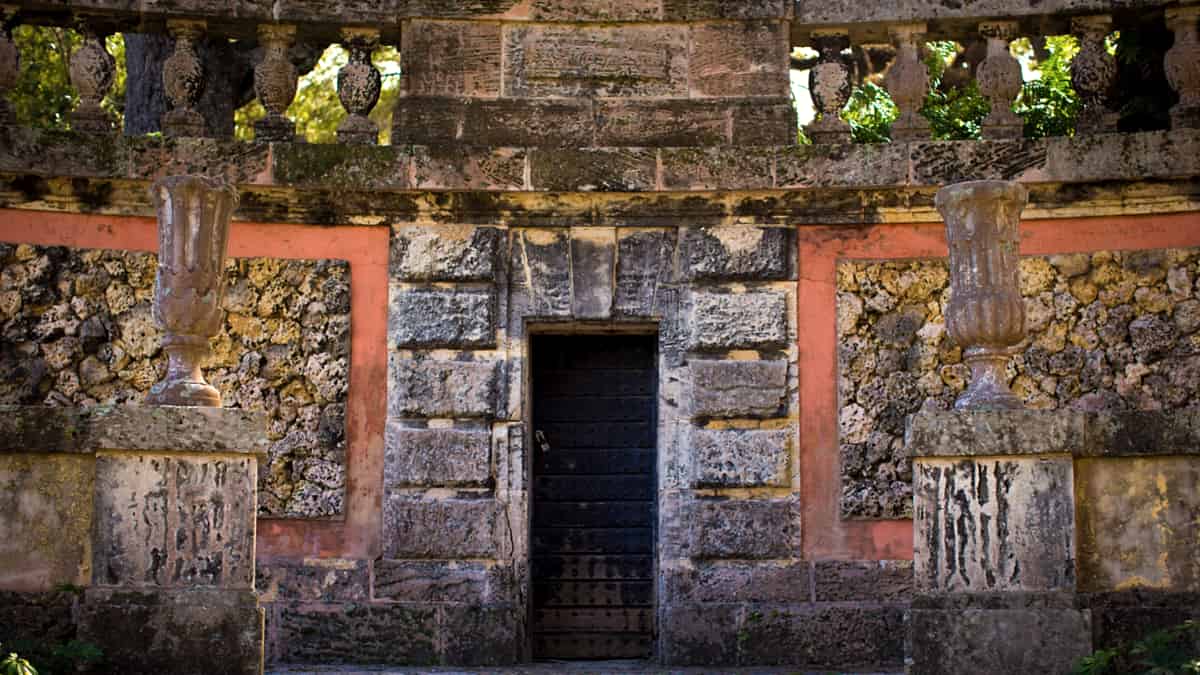 A closed steel gate with a heavy padlock set into a stone wall, photographed straight on in flat light