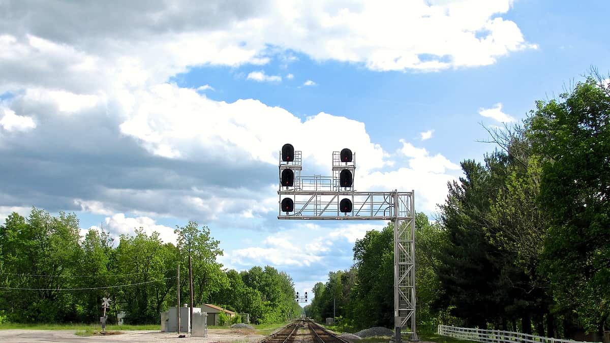 Three parallel railway tracks converging toward a distant switch under an overcast sky